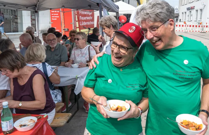 Zwei lachende Personen in grünen T-Shirts halten Schalen mit geschnittenem Gemüse bei einer Schnippeldisko auf dem Lüdenscheider Markt.