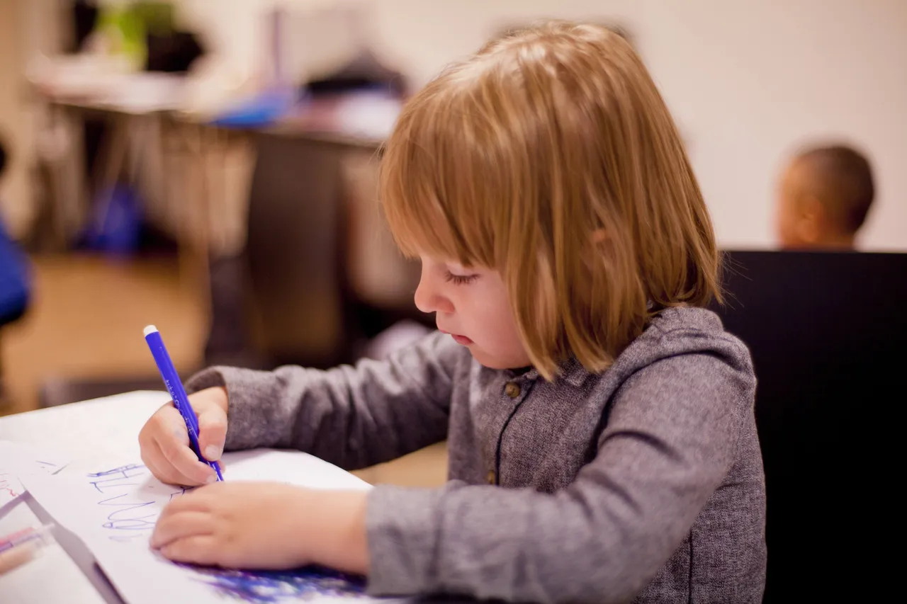 Ein Kind schreibt mit einem blauen Stift auf ein Blatt Papier.