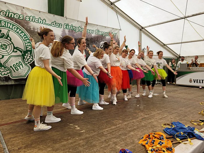 Eine Gruppe von Frauen in weißen T-Shirts und bunten Tüllröcken posiert auf einer Bühne im Festzelt.