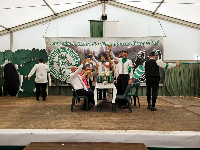 Mitglieder der Biergerichtskommission des Schützenvereins Eiringhausen stoßen auf einer Bühne in einem Festzelt mit Gläsern an.