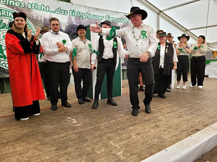 Mitglieder der Biergerichtskommission in Kostümen und mit grünen Rosetten auf einer Bühne im Festzelt.