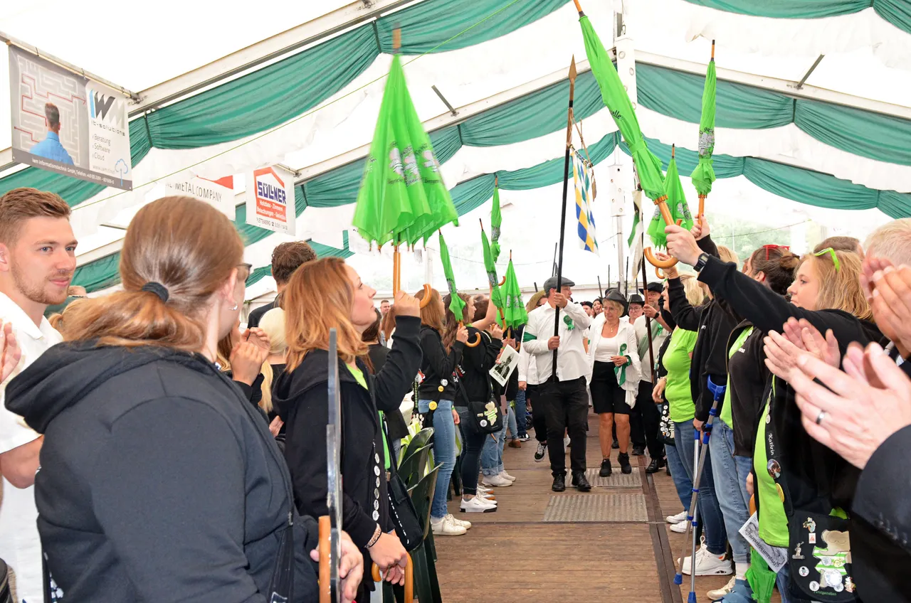 Zuschauer in einem Festzelt halten grüne Fahnen hoch und klatschen während des Schützenfestes in Eiringhausen.