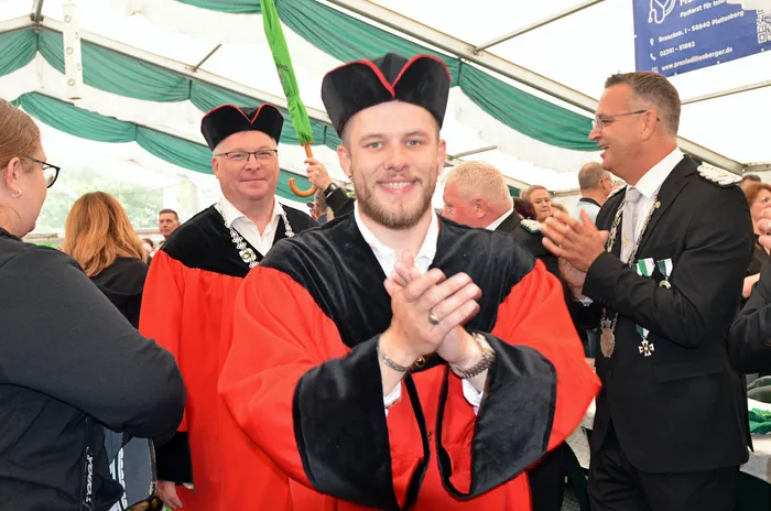 Mitglieder der Biergerichtskommission in rot-schwarzen Gewändern und Hüten klatschen in einem Festzelt.