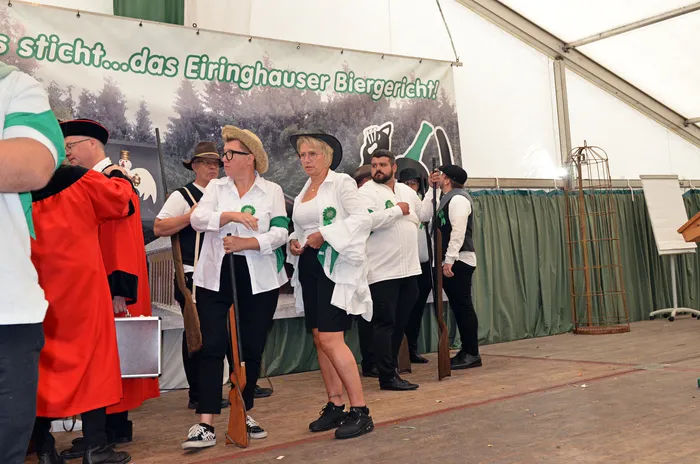Mitglieder der Biergerichtskommission des Schützenvereins Eiringhausen in Kostümen stehen vor einem Banner im Festzelt; einige halten Gewehre.