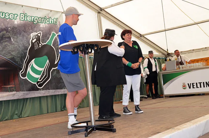 Mitglieder der Biergerichtskommission stehen auf einer Bühne in einem Festzelt vor einem Banner mit der Aufschrift „Biergericht!“.