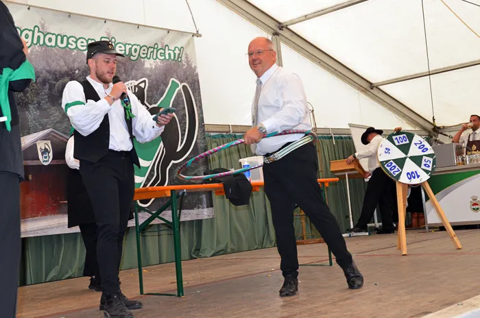 Ein Mann mit Mikrofon und ein Mann mit einem bunten Reifen führen eine Vorführung in einem Festzelt auf.