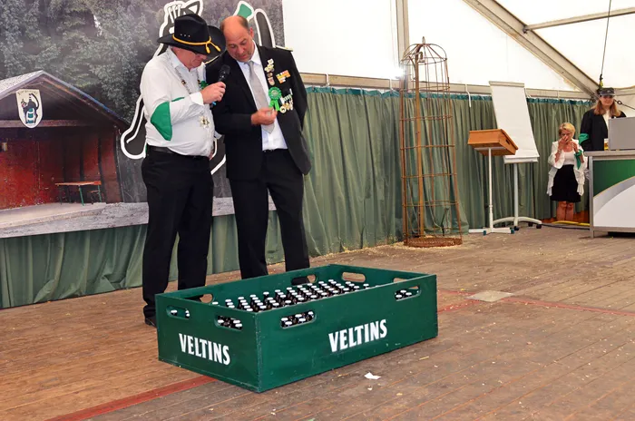 Zwei Männer der Biergerichtskommission stehen in einem Festzelt vor einer grünen Kiste mit Veltins-Bierflaschen.