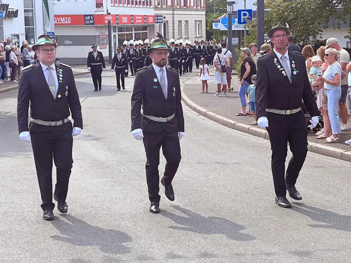 Männer in schwarzen Uniformen mit Hüten, Medaillen und weißen Handschuhen ziehen bei einem Schützenfest in Eiringhausen durch die Straße.
