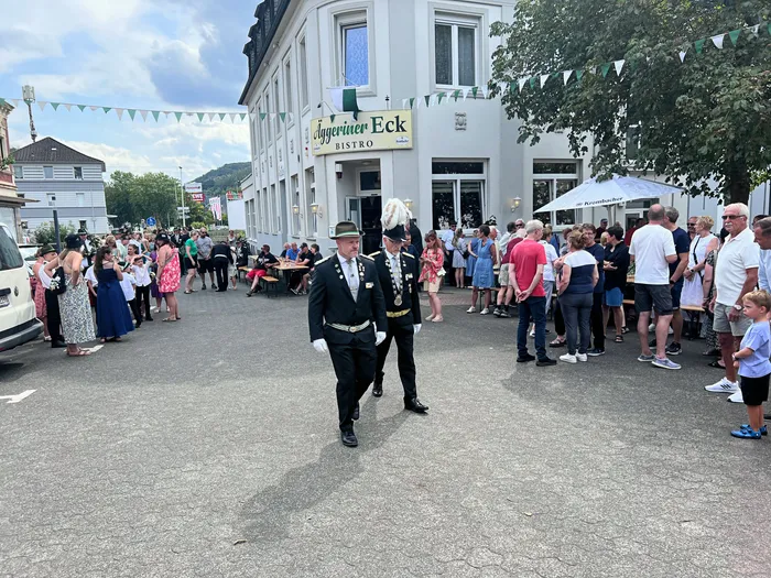 Zwei Männer in traditionellen Schützenuniformen ziehen bei einem Festumzug durch eine Straße vor dem Bistro „Aggeriner Eck“.