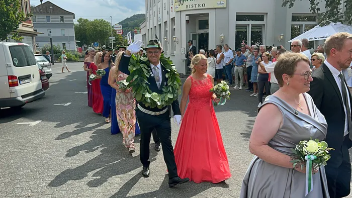 Ein Mann mit einem großen grünen Kranz und eine Frau in einem roten Kleid führen den Festumzug beim Schützenfest in Eiringhausen an.