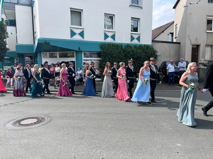 Teilnehmer des Schützenfest-Umzugs in Eiringhausen ziehen in Abendkleidern und Uniformen durch eine Straße.