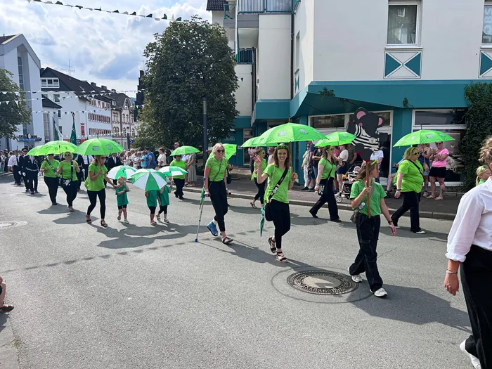 Teilnehmer in grünen T-Shirts ziehen mit grünen Regenschirmen bei einem Festumzug durch eine Straße.