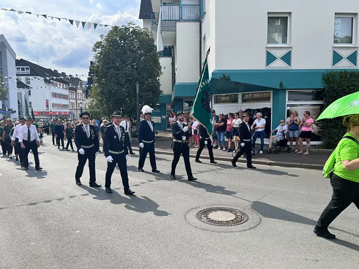 Uniformierte Teilnehmer eines Schützenfest-Festzugs marschieren mit einer grünen Fahne durch eine Straße in Eiringhausen.