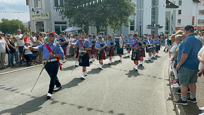 Dudelsackspieler und Trommler in Kilts ziehen bei einem Festumzug durch eine von Zuschauern gesäumte Straße.
