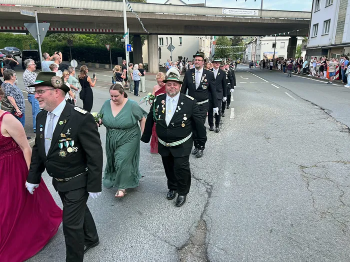 Männer in dunklen Uniformen mit Orden und Hüten sowie Frauen in festlichen Kleidern ziehen bei einem Festumzug durch die Straßen von Eiringhausen.