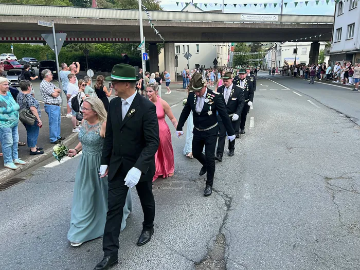 Teilnehmer in festlicher Kleidung und Uniformen mit Orden ziehen bei einem Schützenfest-Umzug durch eine Straße in Eiringhausen.