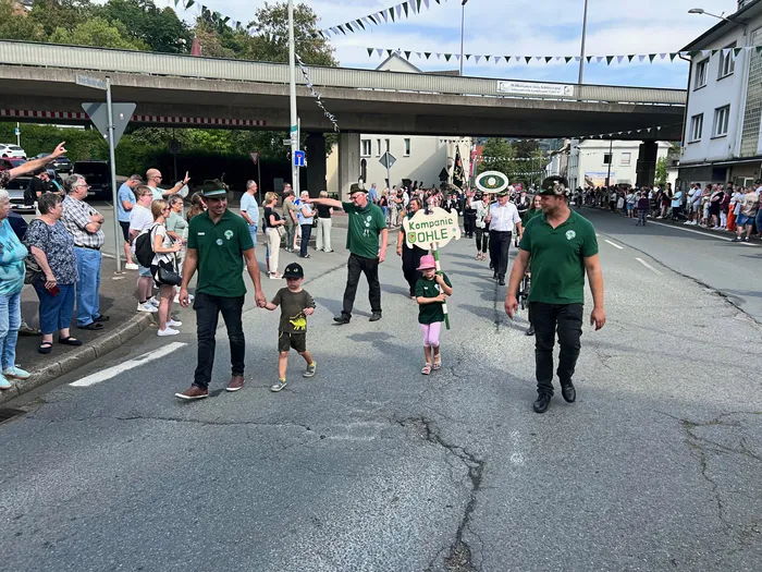 Teilnehmer des Schützenfestes in Eiringhausen in grünen Hemden ziehen bei einem Festumzug durch eine Straße, unter anderem mit einem Schild „KAMPANIE OHLE“.