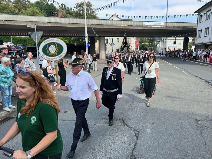 Teilnehmer des Schützenfest-Umzugs in Eiringhausen ziehen durch die Straße, darunter ein Mann mit einem runden Schild der „Kompanie Dorf“.