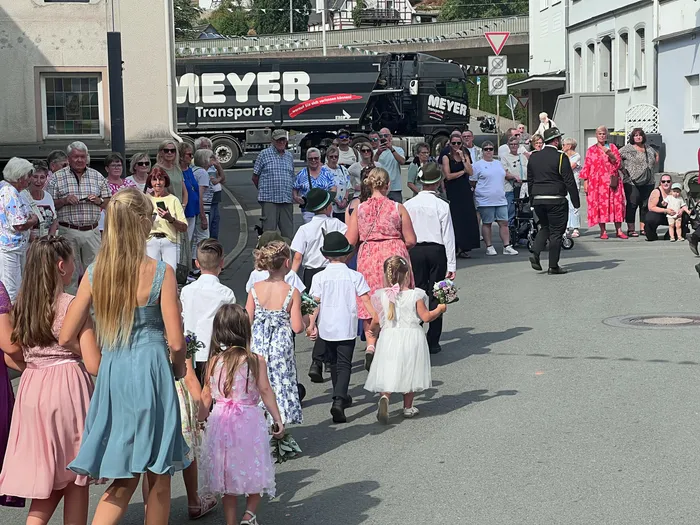 Kinder in festlicher Kleidung ziehen bei einem Schützenfest-Umzug durch die Straße, während Zuschauer am Rand stehen.