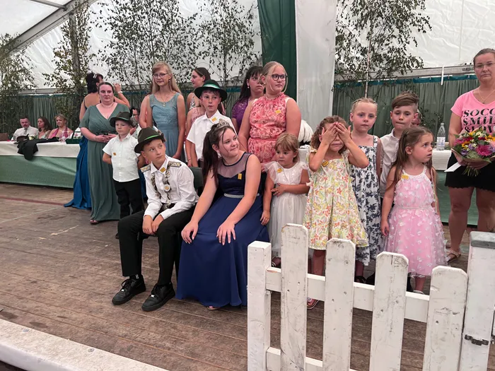 Eine Gruppe von Kindern und Jugendlichen in festlicher Kleidung posiert hinter einem weißen Lattenzaun.