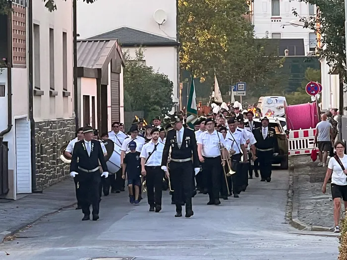 Mitglieder des Schützenvereins in dunklen Uniformen und weißen Hemden marschieren mit Musikinstrumenten durch eine Straße.