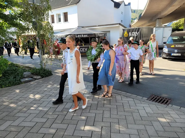 Kinder in festlicher Kleidung ziehen bei einem Schützenfest in Eiringhausen in einer Prozession durch die Straße; ein Junge trägt einen grünen Kranz.