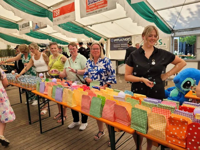 Mehrere Frauen stehen hinter einem langen Tisch mit vielen bunten Geschenktüten unter einem Festzelt beim Schützenfest Eiringhausen.
