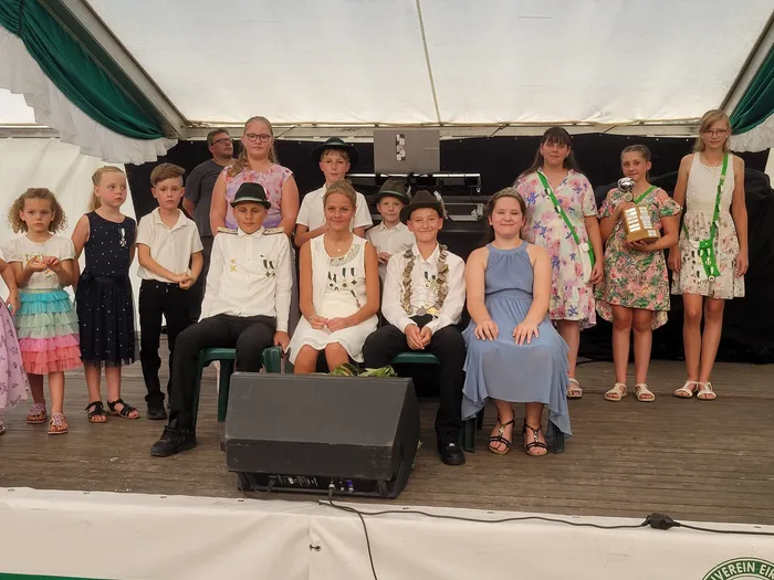 Eine Gruppe von Kindern in festlicher Kleidung mit Blumenkränzen und einer Trophäe posiert auf einer Bühne beim Schützenfest Eiringhausen.