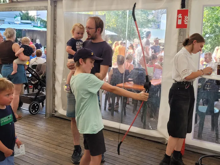 Ein Junge in einem hellgrünen T-Shirt hält einen roten Bogen in einem Festzelt.