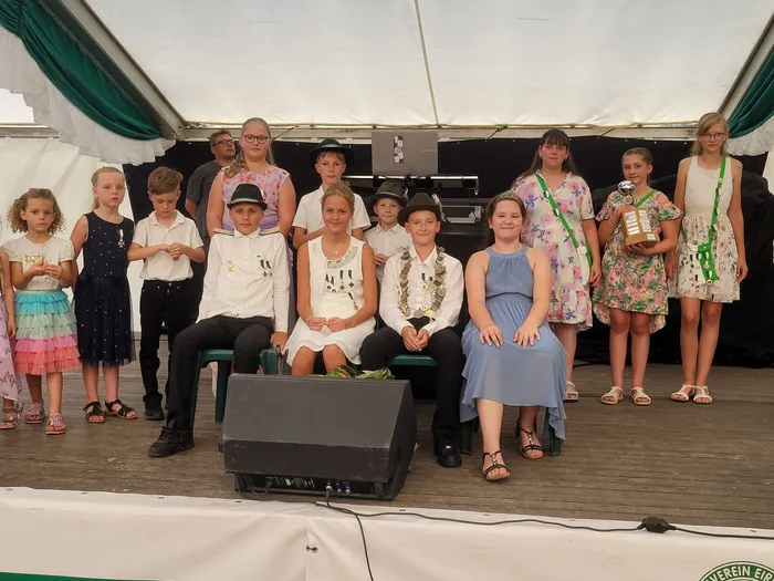 Eine Gruppe von Kindern in festlicher Kleidung posiert mit Medaillen und einem Pokal auf einer Bühne beim Schützenfest Eiringhausen.