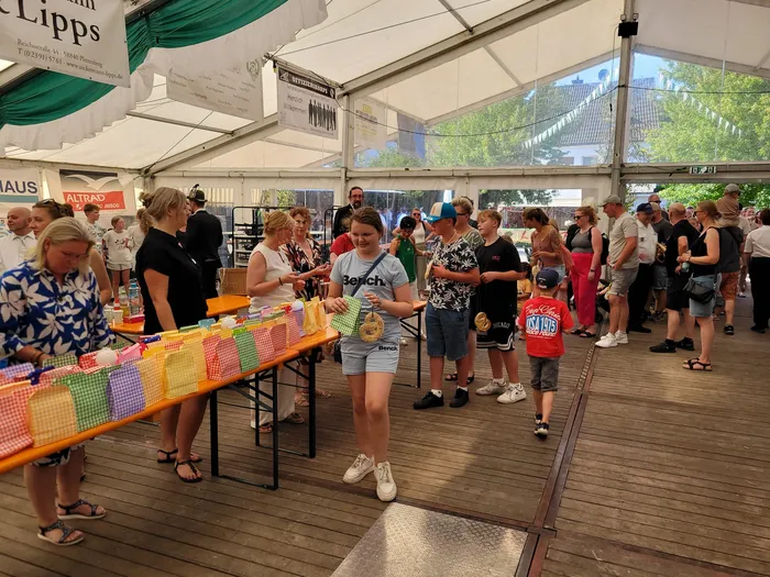 Unter einem großen Festzelt stehen Kinder und Erwachsene an einem Tisch mit vielen bunten Stoffbeuteln.