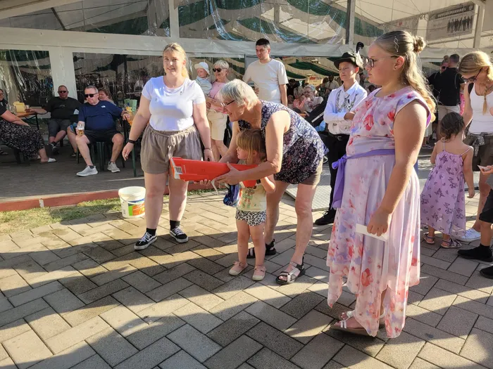 Beim Kids Day des Schützenfestes in Eiringhausen überreicht eine Frau einem Kind einen roten Gegenstand unter einem Festzelt.