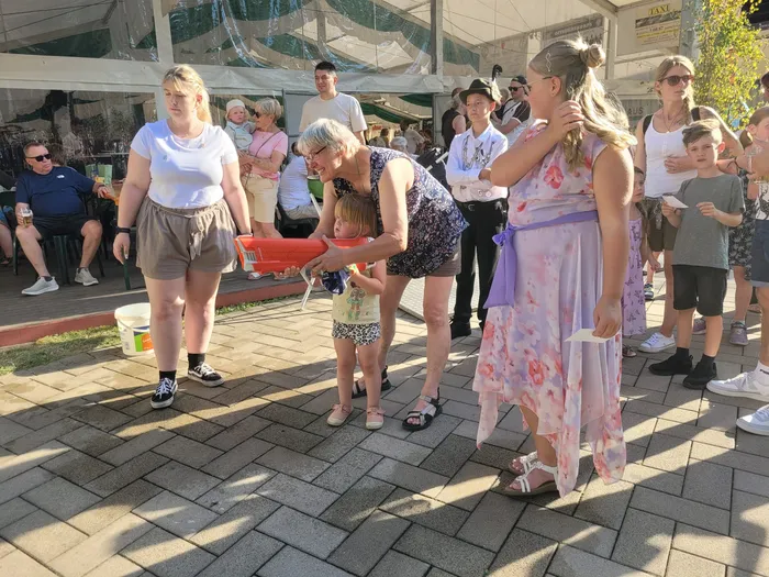 Bei einem Schützenfest beugt sich eine Frau zu einem kleinen Kind, während ein Mädchen in einem hellen Blumenkleid im Vordergrund steht.
