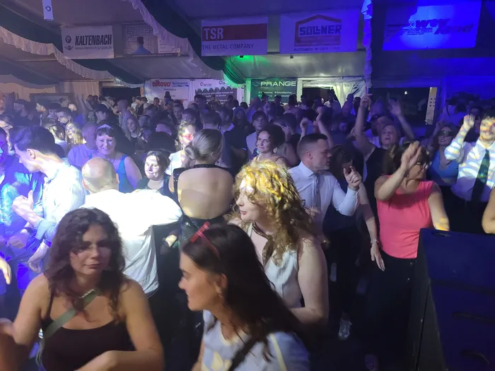Eine tanzende Menschenmenge in einem Festzelt mit Werbebannern im Hintergrund.