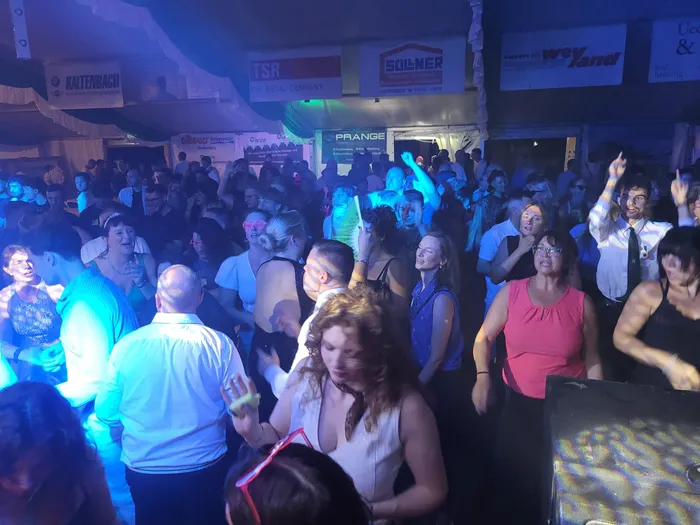 Menschen tanzen auf einer belebten Tanzfläche in einem Festzelt unter blauem Licht.