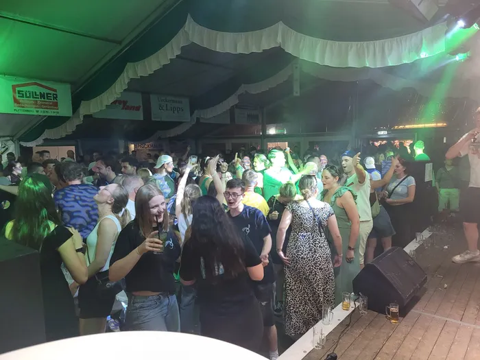 Eine Menschenmenge tanzt und feiert in einem Festzelt unter grünem Licht.