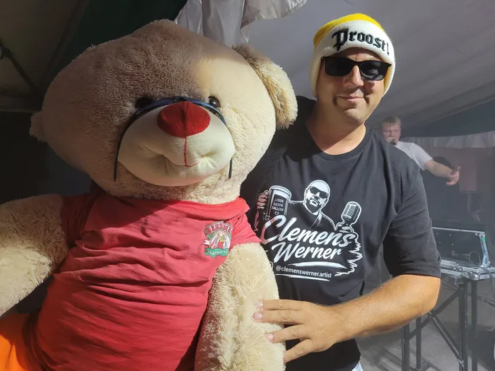 Clemens Werner posiert mit einem großen Teddybären in einem Festzelt.