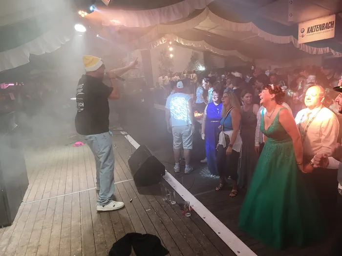 Clemens Werner performt mit einem Mikrofon auf einer Bühne in einem verrauchten Festzelt vor einer Menschenmenge.