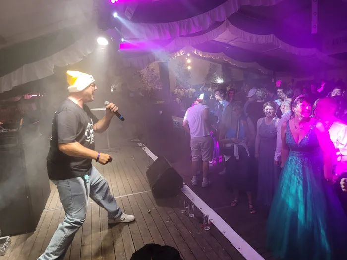Clemens Werner singt mit einem Mikrofon in einem lila beleuchteten Festzelt vor einer Menschenmenge.