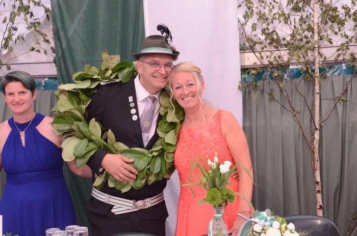 Sascha Kasel mit grünem Hut und großem Blattkranz lächelt gemeinsam mit Alexandra Langenberg-Kasel in einem orangefarbenen Kleid.