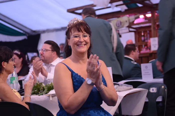 Eine lächelnde Frau mit Diadem und blauem Kleid klatscht während einer Zeremonie im Festzelt.