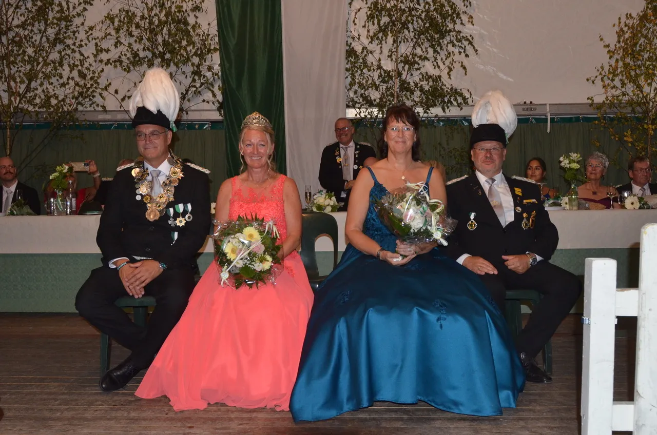 Zwei Männer in Uniform mit weißen Federbüschen und zwei Frauen in festlichen Kleidern sitzen bei der Krönung des Schützenvereins Eiringhausen.