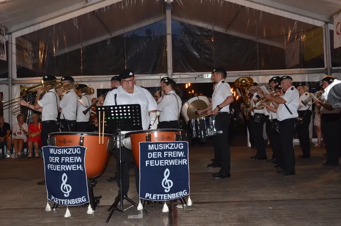 Der Musikzug der Freiwilligen Feuerwehr Plettenberg spielt mit Blasinstrumenten und Trommeln in einem Festzelt.