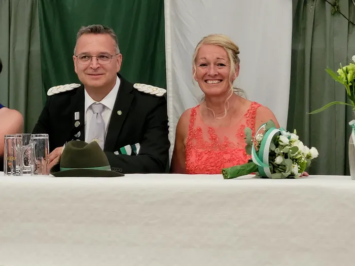 Marc und Tanja Stahlschmidt sitzen an einem weiß gedeckten Tisch; er trägt eine dunkle Uniform, sie ein korallenfarbenes Spitzenkleid.