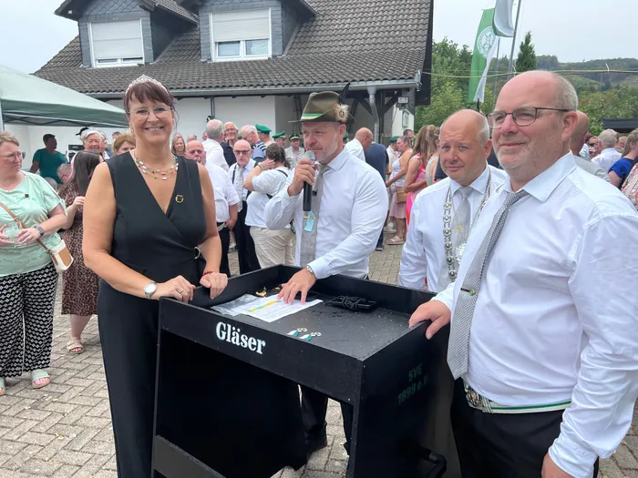 Sascha Kasel spricht bei einem Schützenfest in Eiringhausen in ein Mikrofon, umgeben von Teilnehmern an einem schwarzen Tisch.