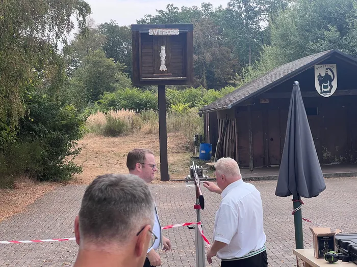 Ein Mann zielt bei einem Schützenfest mit einem Gewehr auf eine hölzerne Zielscheibe mit einer kleinen Vogelfigur.