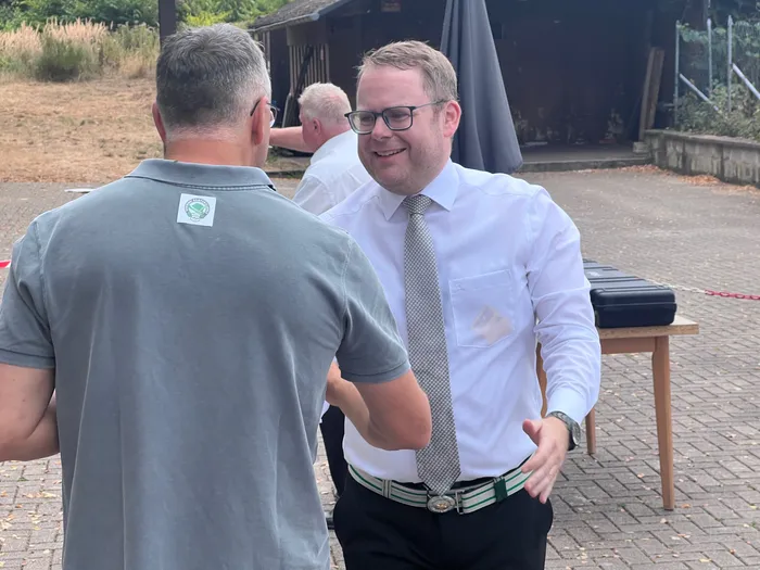 Sascha Kasel im weißen Hemd und Krawatte lächelt einem Mann beim Schützenfest Eiringhausen entgegen.