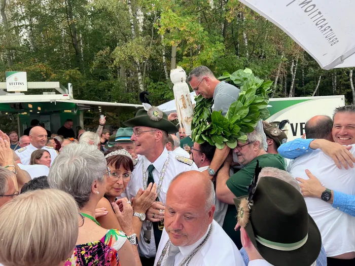 Sascha Kasel wird beim Schützenfest Eiringhausen inmitten einer feiernden Menge mit einem großen grünen Kranz und einer Vogelfigur gefeiert.