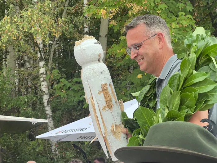 Sascha Kasel lächelt mit einem grünen Kranz um den Hals und hält die hölzerne Vogelfigur.