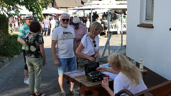 Beim Schützenfest-Warm-up der Kompanie Ohle betrachtet eine Frau an einem Holztisch eine kleine schwarze Box, während ein Mann daneben steht.